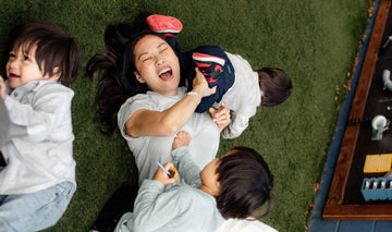 Mom laughing while playing on the grass with her young children, enjoying quality family time outdoors.